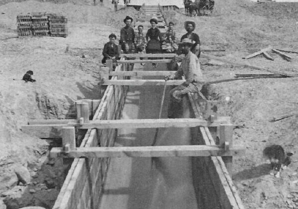 A wooden flume conveys water down the big drop below the division of the Highline and Mainline laterals of the Grand River Ditch about 1883